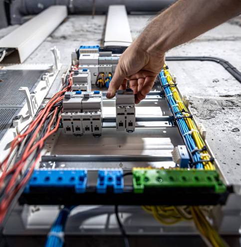 A male electrician works in a switchboard with an electrical connecting cable. Voltage switchboard with circuit breakers are in the ON and OF positions in the big electric box for electrical distribution panel, and temporary electric cables are switched.